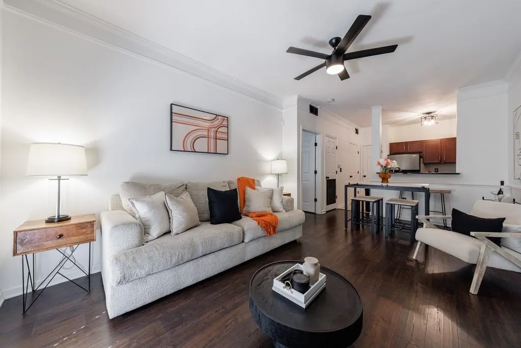 Living room featuring dark wood-type flooring, ornamental molding, and ceiling fan