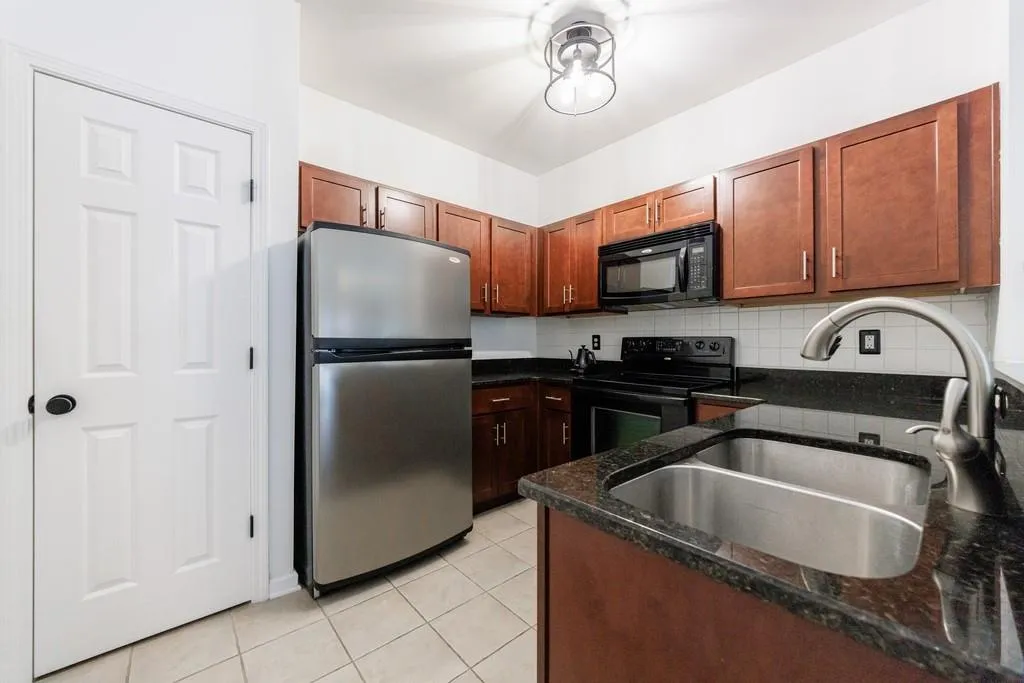 Kitchen with sink, black appliances, light tile patterned floors, dark stone countertops, and backsplash