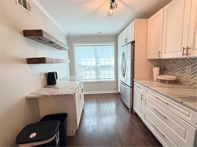 White shaker-style cabinetry with gold-tone hardware, wood-finish flooring, stainless steel French door refrigerator, white marble-style countertops, and a chevron pattern tile backsplash