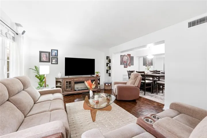 Spacious living area featuring dark wood-finish flooring, white walls, and an open concept to a dining space
