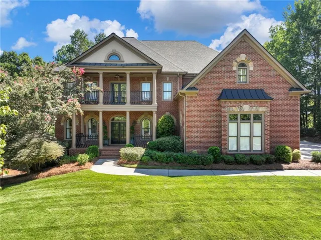Brick exterior with a prominent arched entry, double-story porch with columns, and wrought iron balcony railings