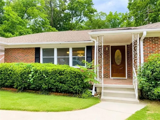 Brick exterior featuring a wood-panel entry door with an oval glass insert, white scrolled metal porch columns, three-step concrete entry, and a manicured front lawn