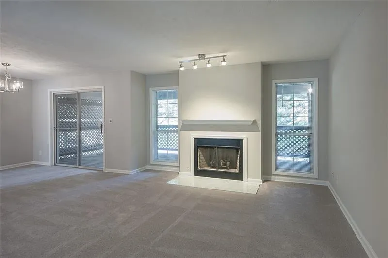 Unfurnished living room with carpet floors, healthy amount of natural light, a chandelier, and a fireplace with flush hearth