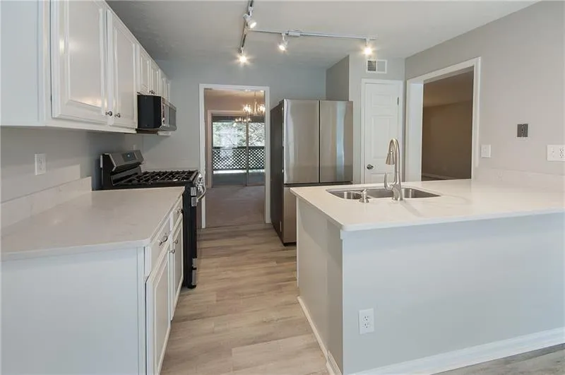 Kitchen featuring appliances with stainless steel finishes, white cabinets, a peninsula, track lighting, and a chandelier
