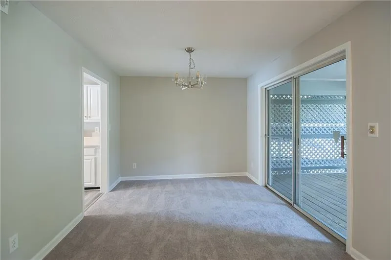 Carpeted spare room featuring a chandelier and baseboards