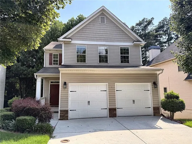 Two-story exterior with light-toned siding, a prominent front porch, a two-car garage, and mature landscaping