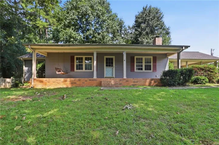 Front exterior with light blue siding, red brick foundation, and a covered porch