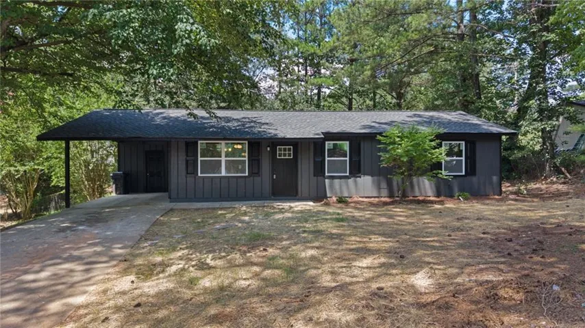 Ranch-style exterior featuring dark vertical siding, white-framed windows with black shutters, and a covered carport