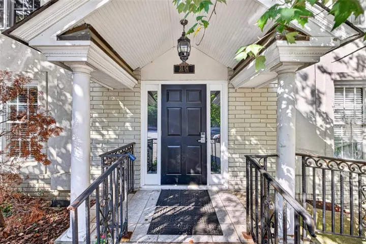 Entryway featuring a paneled door with sidelights, brick exterior, columned portico, and wrought iron railings