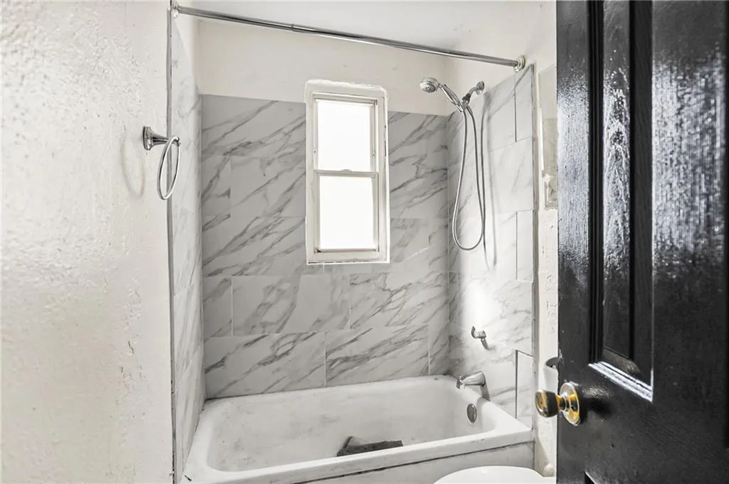 Bathroom featuring washtub / shower combination and a textured wall