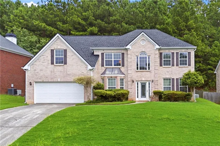 Two-story residence featuring a light brick exterior, dark-toned shutters, and a two-car garage