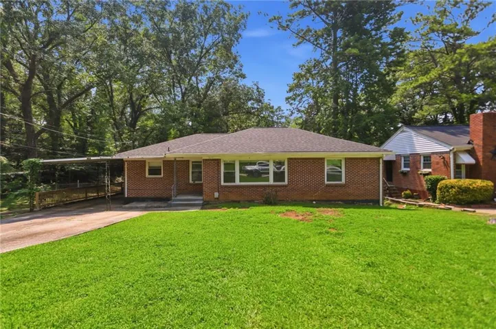 Brick ranch home featuring a covered carport, mature trees, a front lawn, and a paved driveway