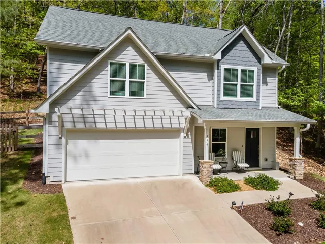 The property features a light-colored exterior with a grey shingled roof, a front porch with stone-clad columns, and an integrated garage