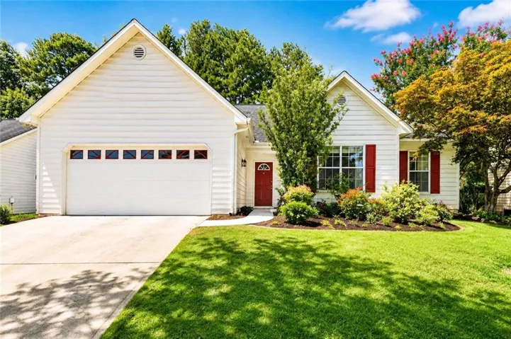 White siding exterior with a red front door, red window shutters, a two-car garage, and landscaped planting beds