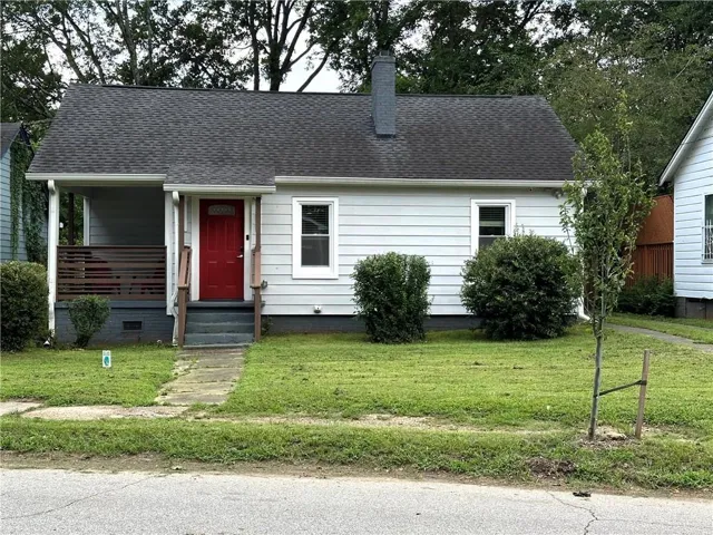 Exterior featuring white siding, a prominent red entry door, a covered front porch, and a dark shingle roof