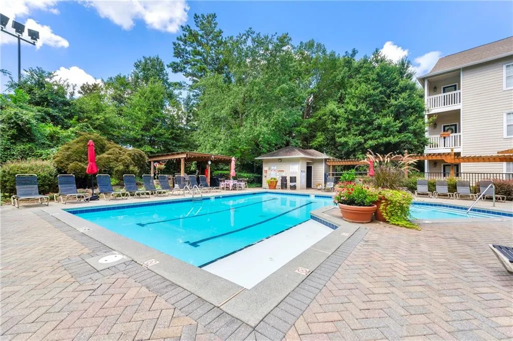Community pool with a patio, view of scattered trees, and an outbuilding