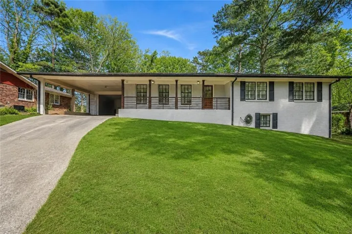 White painted brick exterior featuring a covered carport, concrete driveway, front porch with black railings, and shuttered windows
