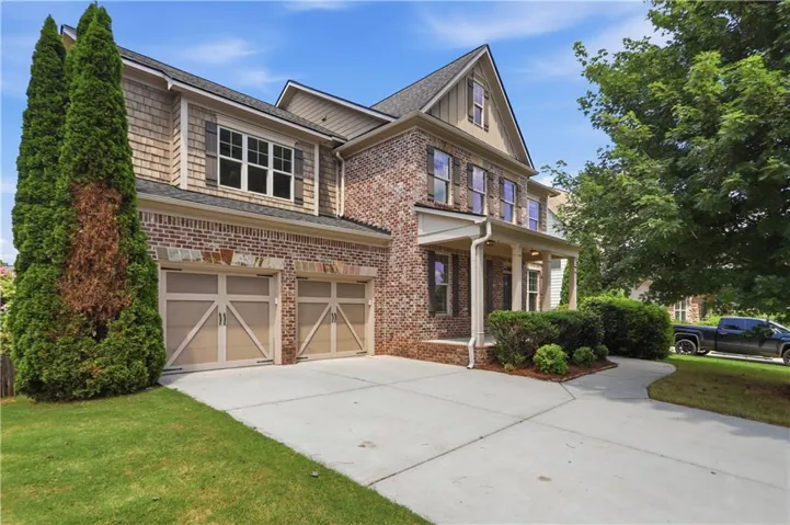 Brick and shingle exterior featuring a covered front porch with columns, a concrete driveway, and two carriage-style garage doors