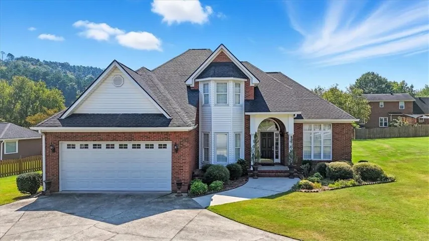 Two-story residence featuring a brick and white siding exterior with a prominent arched entry, bay window, and a two-car garage