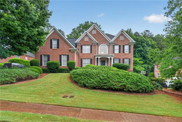 Brick exterior with multiple gables, arched window, covered entryway, and mature landscaping