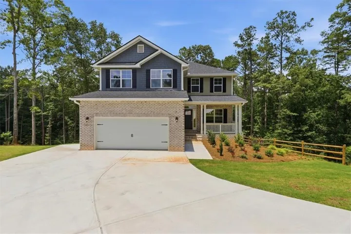 Two-story residence featuring a brick and siding facade, a covered porch, an attached garage, and a concrete driveway