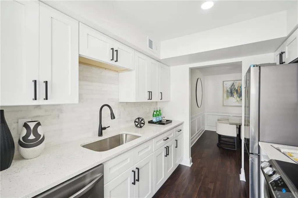 Kitchen with white cabinetry, light stone countertops, visible vents, appliances with stainless steel finishes, and a sink