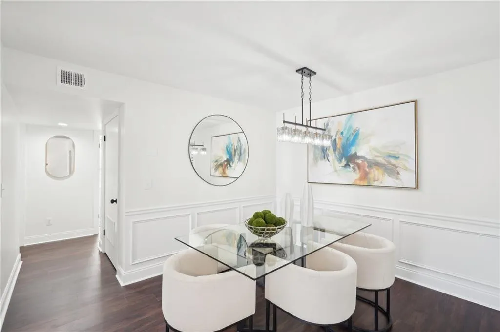Dining space with a decorative wall, dark wood-style flooring, wainscoting, and visible vents