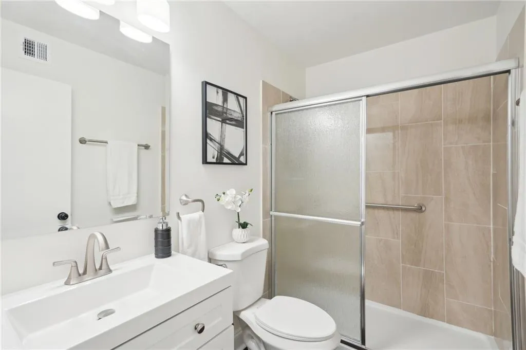 Bathroom with toilet, tiled shower, vanity, and visible vents