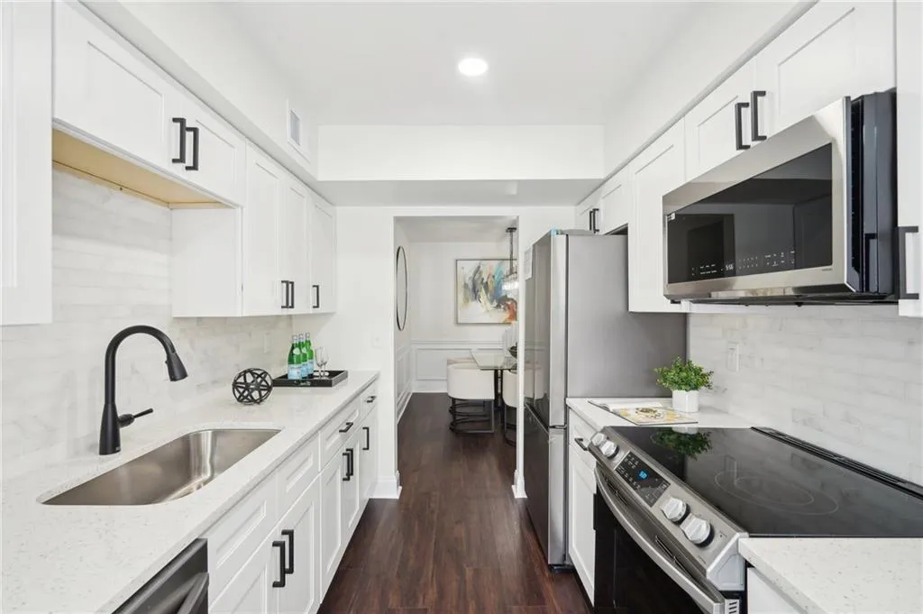 Kitchen featuring white cabinets, appliances with stainless steel finishes, light stone counters, a sink, and backsplash