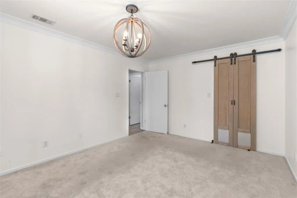 Unfurnished bedroom with crown molding, a barn door, a chandelier, and carpet flooring