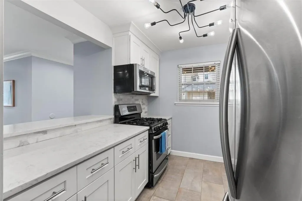 Kitchen featuring stainless steel appliances, white cabinets, tiled backsplash, light stone counters,