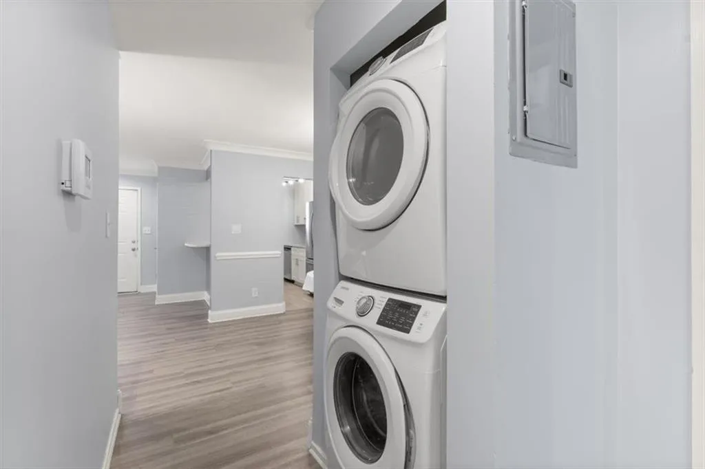 Laundry area featuring crown molding, light wood-style floors, stacked washer / dryer, and electric panel