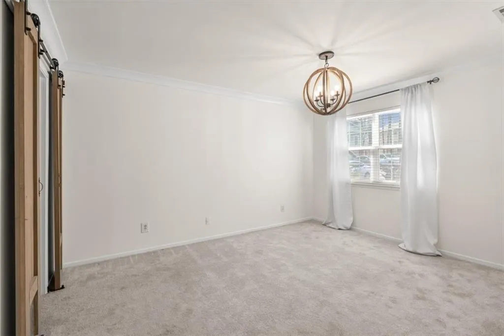 Spare room featuring a barn door, carpet floors, crown molding, and an updated chandelier