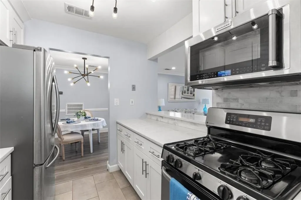 Kitchen with stainless steel appliances, white cabinets, light stone countertops, and eye catching light fixture