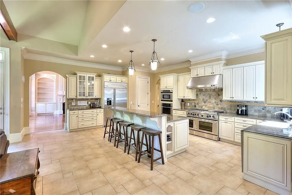 Kitchen featuring high quality appliances, tasteful backsplash, pendant lighting, dark stone countertops, and a kitchen island