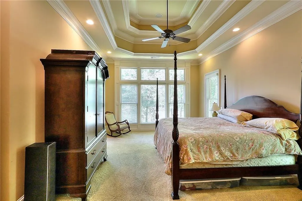Carpeted bedroom featuring ornamental molding, multiple windows, ceiling fan, and a raised ceiling