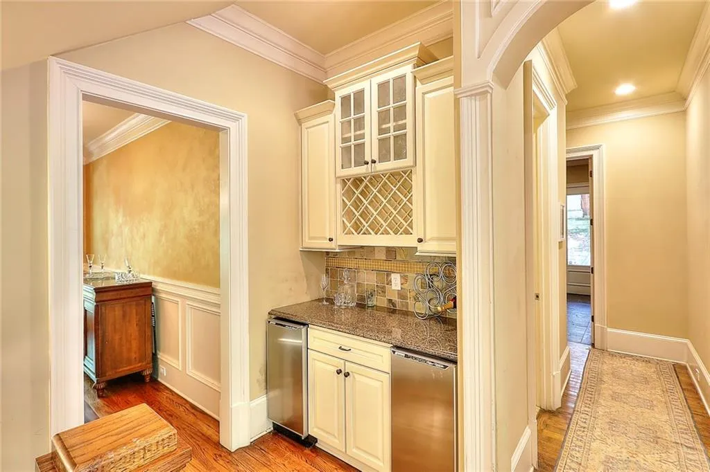 Bar featuring tasteful backsplash, dark stone counters, dishwasher, light wood-type flooring, and crown molding