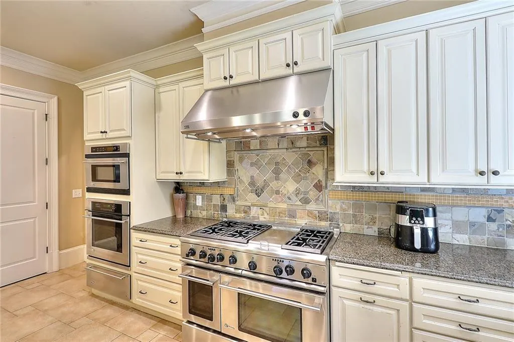 Kitchen with tasteful backsplash, dark stone countertops, appliances with stainless steel finishes, light tile floors, and ornamental molding
