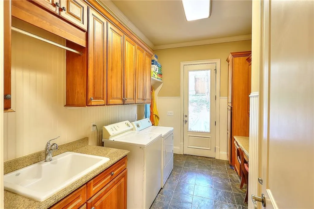 Laundry room featuring cabinets, dark tile flooring, sink, washing machine and dryer, and crown molding