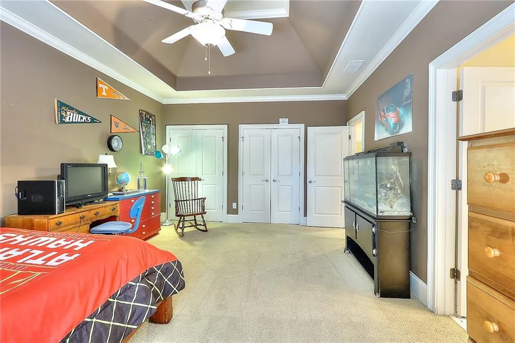 Bedroom featuring light carpet, a raised ceiling, ornamental molding, ceiling fan, and two closets