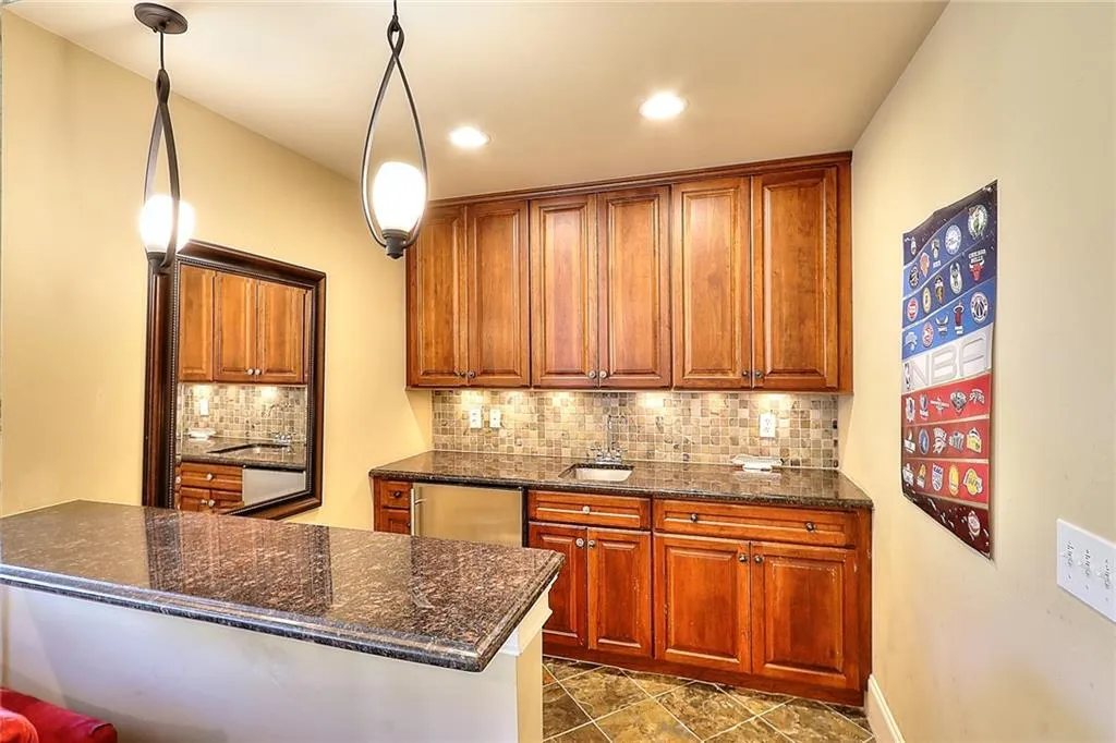 Kitchen with tasteful backsplash, dark stone countertops, stainless steel dishwasher, dark tile floors, and hanging light fixtures