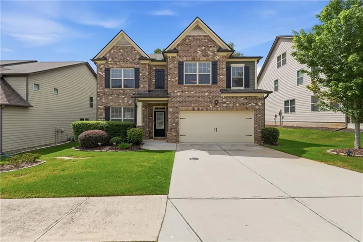 Brick Colonial two-story featuring a welcoming front elevation with peaked gable rooflines, multiple windows with dark shutters, and a two-car garage