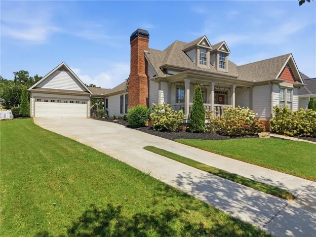 Siding exterior with dormer windows, a covered front porch, an attached garage, and a brick chimney
