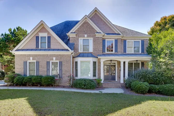 Brick exterior with gabled rooflines, bay window, covered porch, and mature landscaping