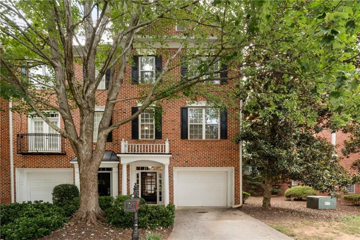 Brick townhome facade featuring black shutters, a white columned portico, and a white balcony with black iron railing