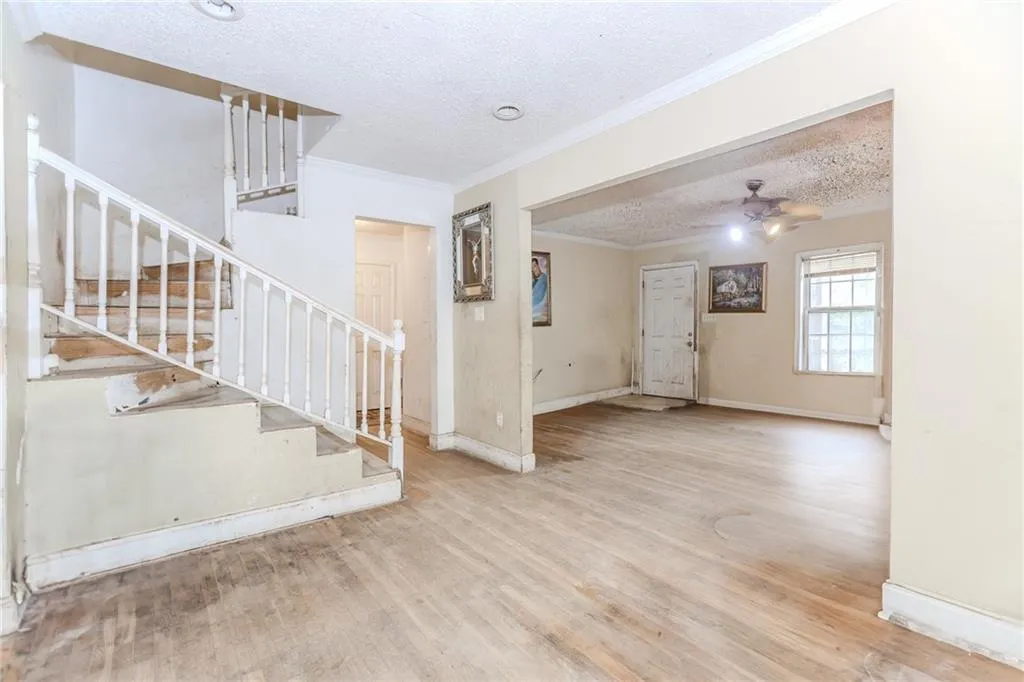 Unfurnished living room featuring a textured ceiling, crown molding, light wood-style flooring, ceiling fan, and stairs