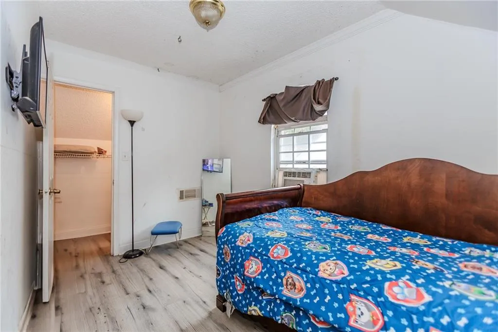 Bedroom featuring wood finished floors, a textured ceiling, crown molding, and a spacious closet