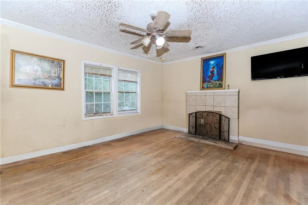 Unfurnished living room with crown molding, a fireplace, ceiling fan, wood finished floors, and a textured ceiling