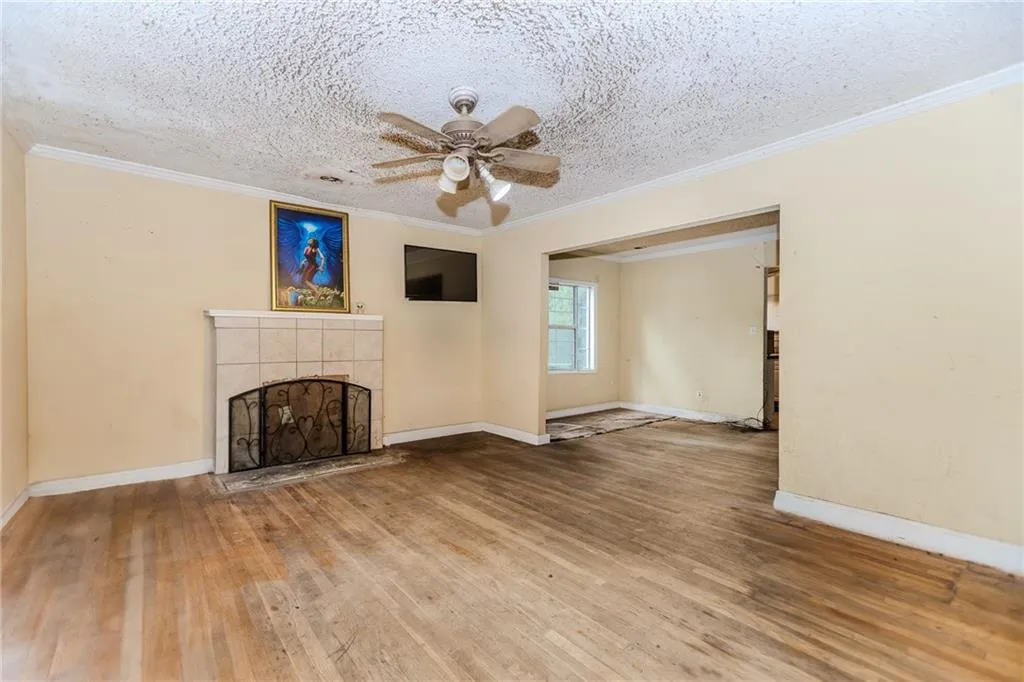 Unfurnished living room with ornamental molding, ceiling fan, a textured ceiling, hardwood / wood-style flooring, and a tiled fireplace