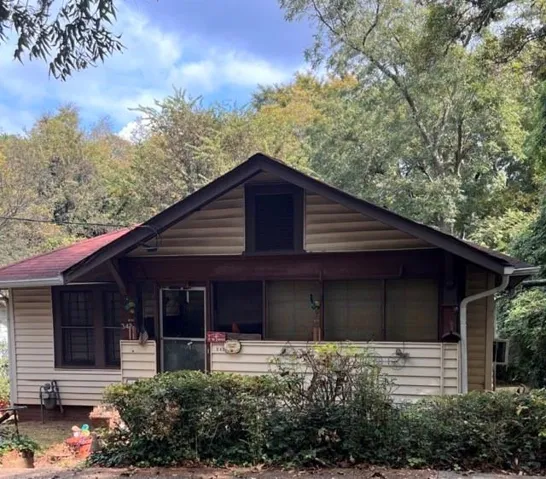 Craftsman-style home featuring light beige siding, a red shingle roof, and a covered front porch with a dark trim